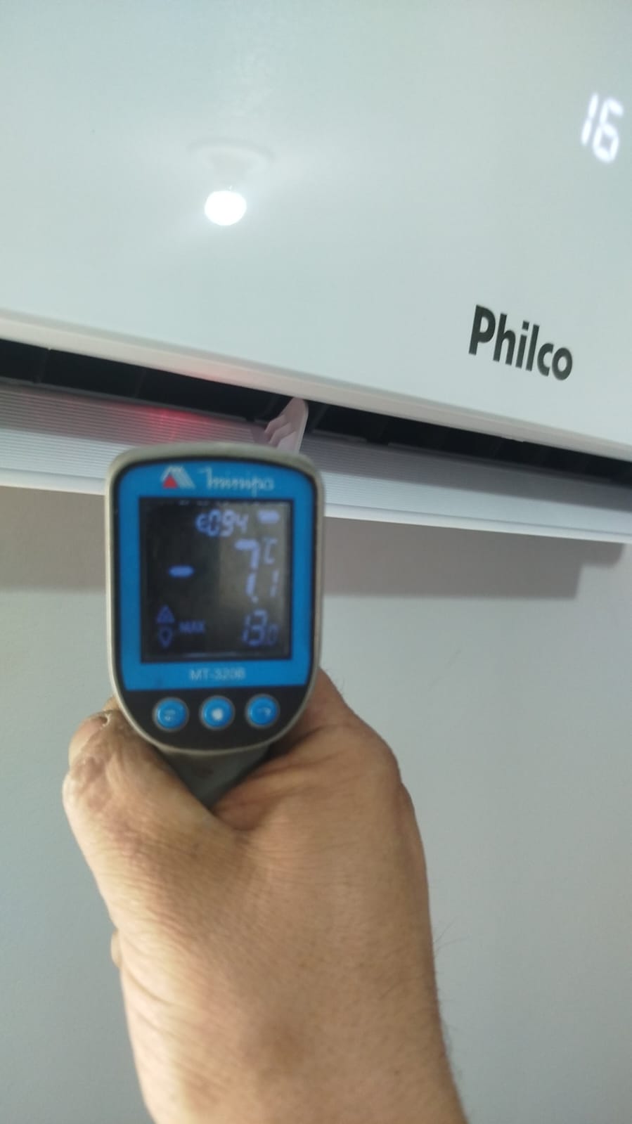 mão segurando um termômetro infravermelho medindo a saída de ar de um ar-condicionado split Philco — texto: P