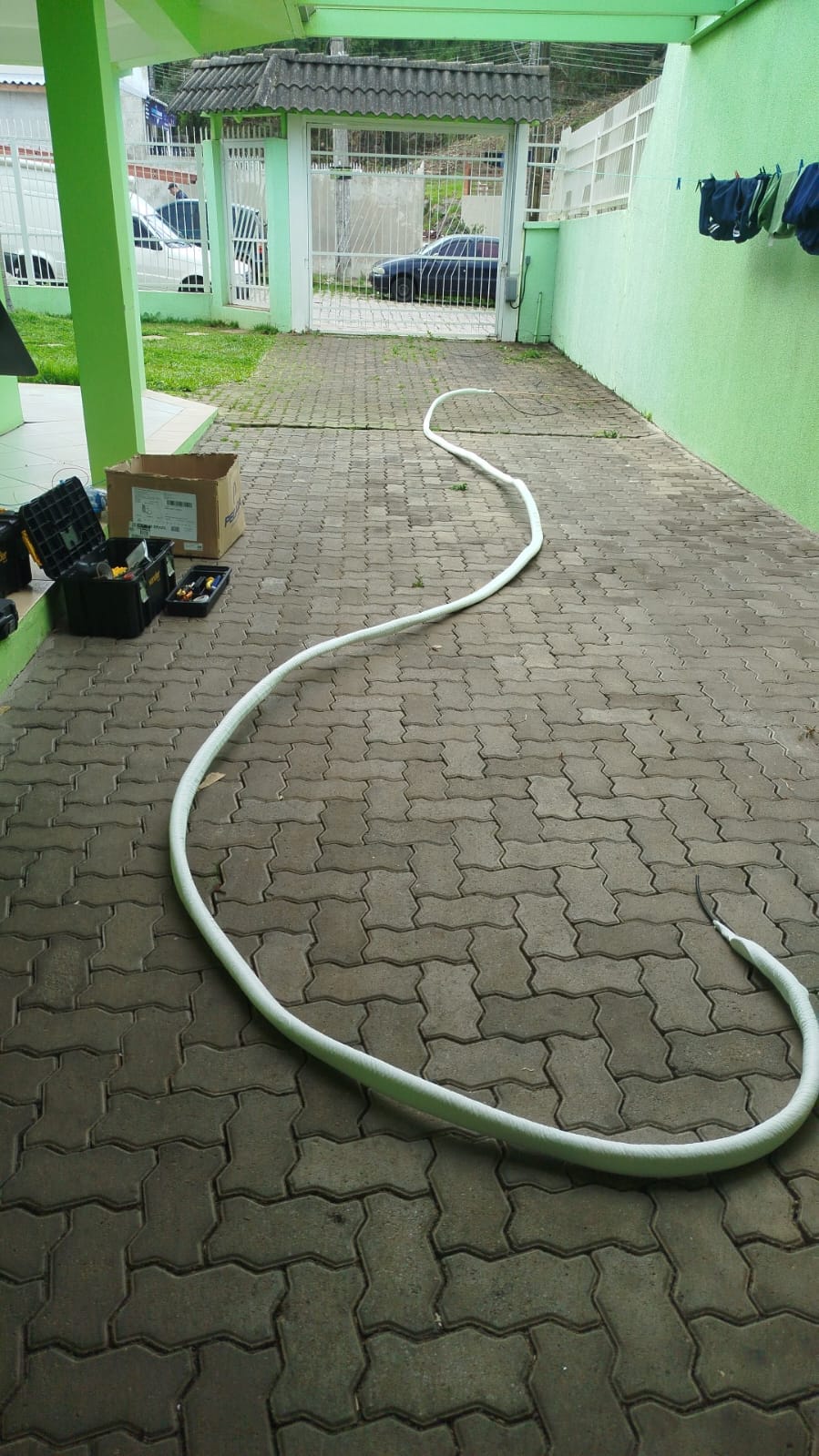 longa tubulação branca de ar-condicionado serpenteando pelo piso intertravado de um pátio, com caixas de ferra
