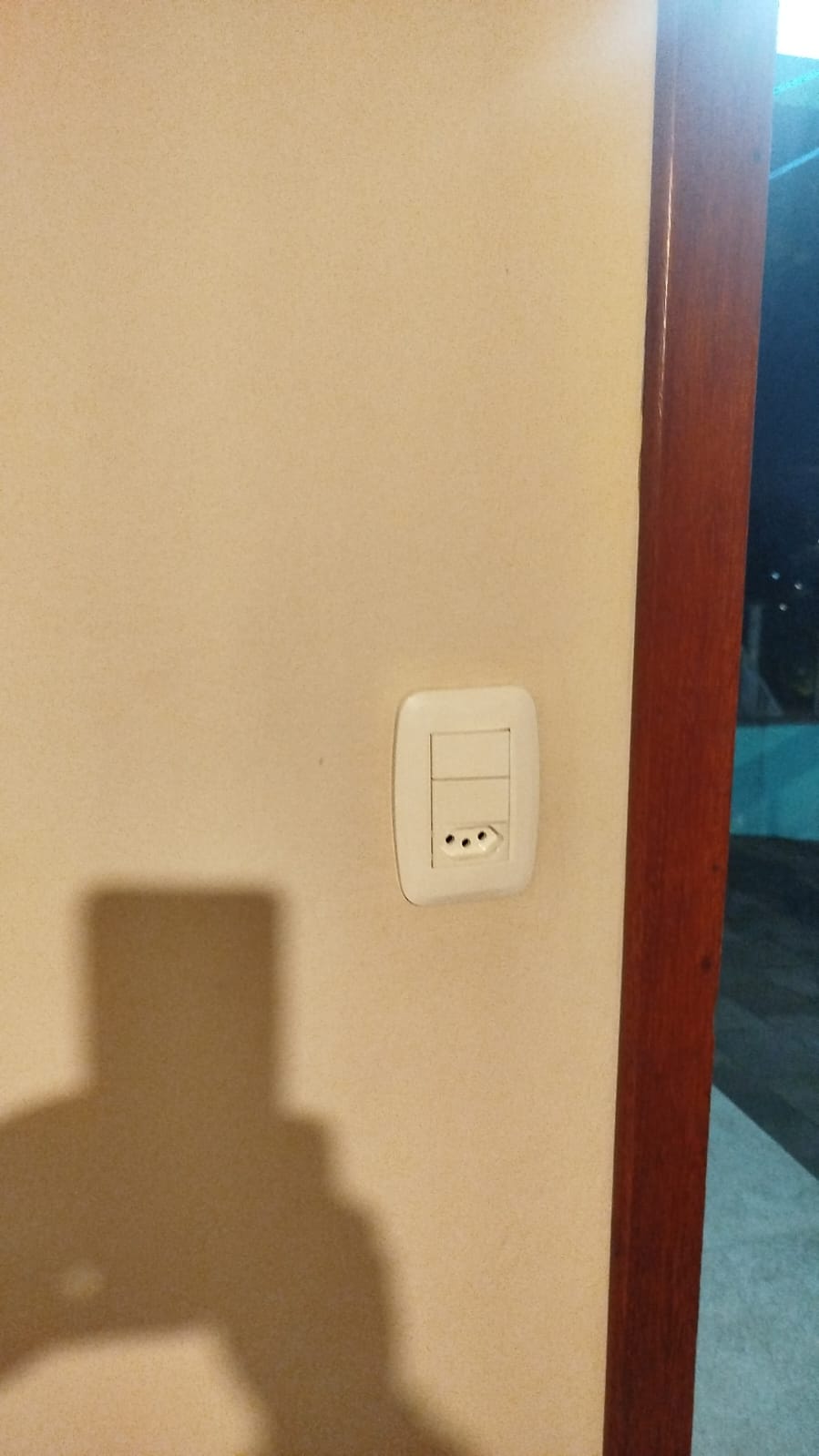 tomada e interruptor brancos numa parede bege, com a sombra de quem tira a foto — texto: 