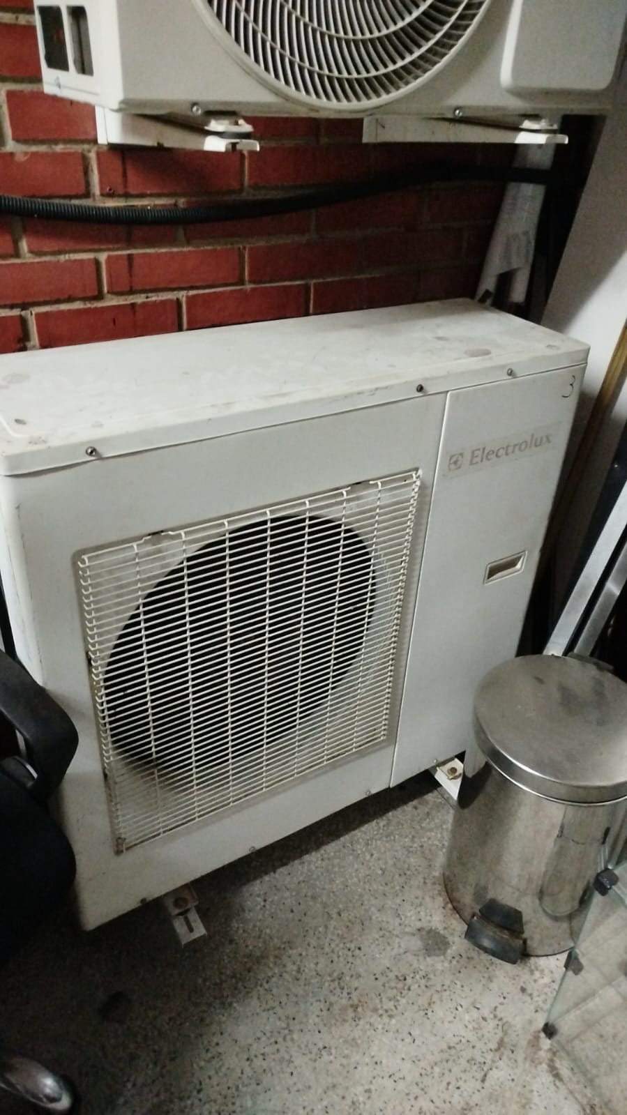 condensadora de ar-condicionado Electrolux no chão ao lado de um lixeiro inox, com evaporador montado na pared
